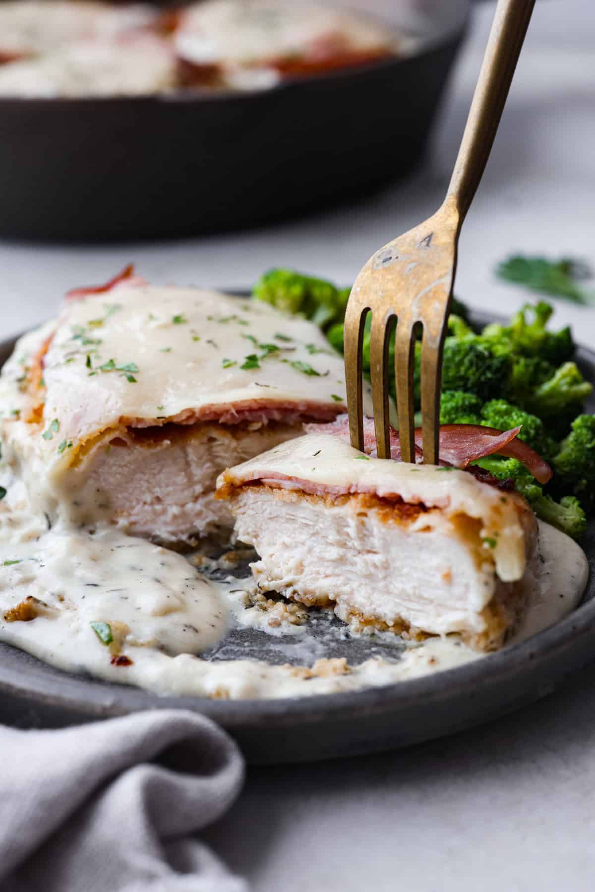 Skillet chicken cordon bleu is one of those recipes my whole family loves. You can't beat the creamy sauce, crispy chicken, and smokey ham, all covered in melty Swiss cheese. Side shot of plated chicken cordon blue cut in half with a fork sticking out of a bite.