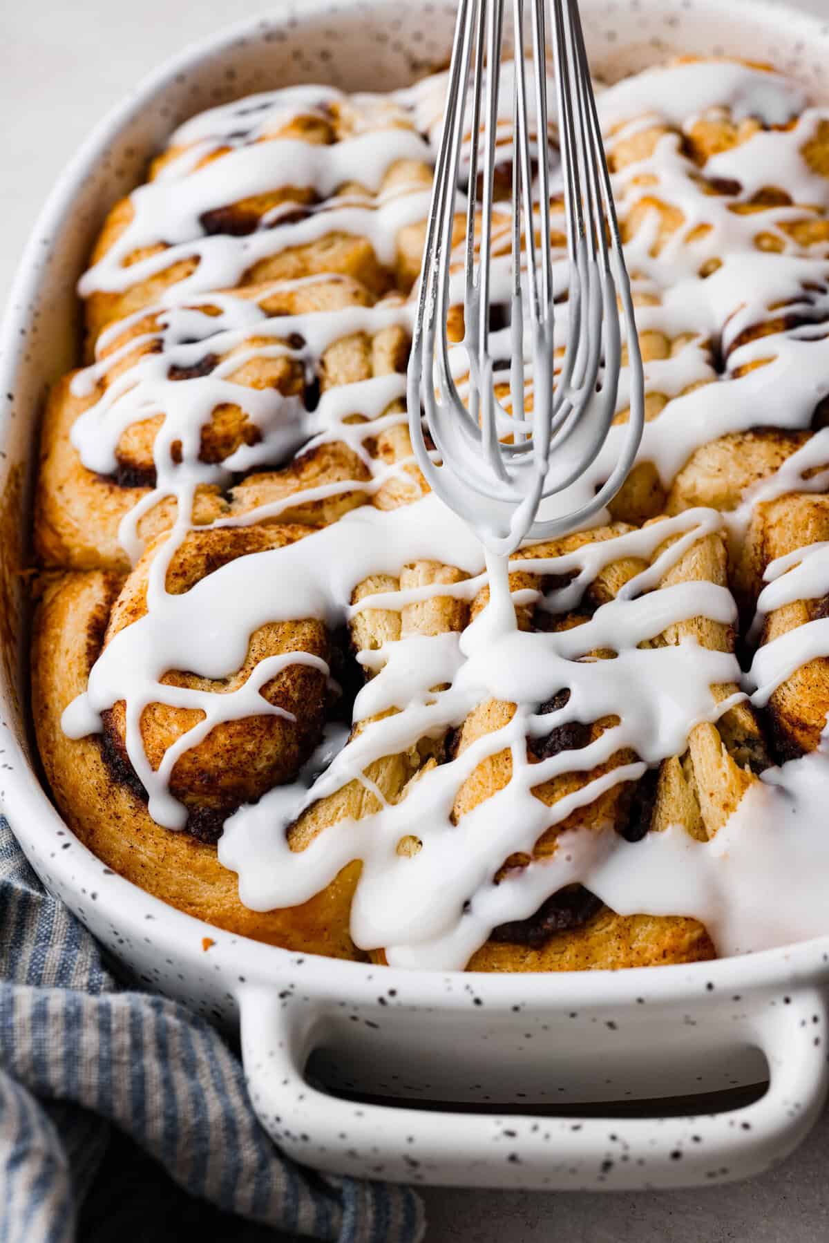 Biscuit Cinnamon Rolls are the most amazing twist on a classic! They are perfectly light, fluffy, and packed with cinnamon. The texture is more flakey and moist than traditional cinnamon rolls! Whether it’s for a cozy weekend breakfast or a holiday brunch, these hit the spot! Close up shot of someone drizzling glaze over the biscuit cinnamon rolls.