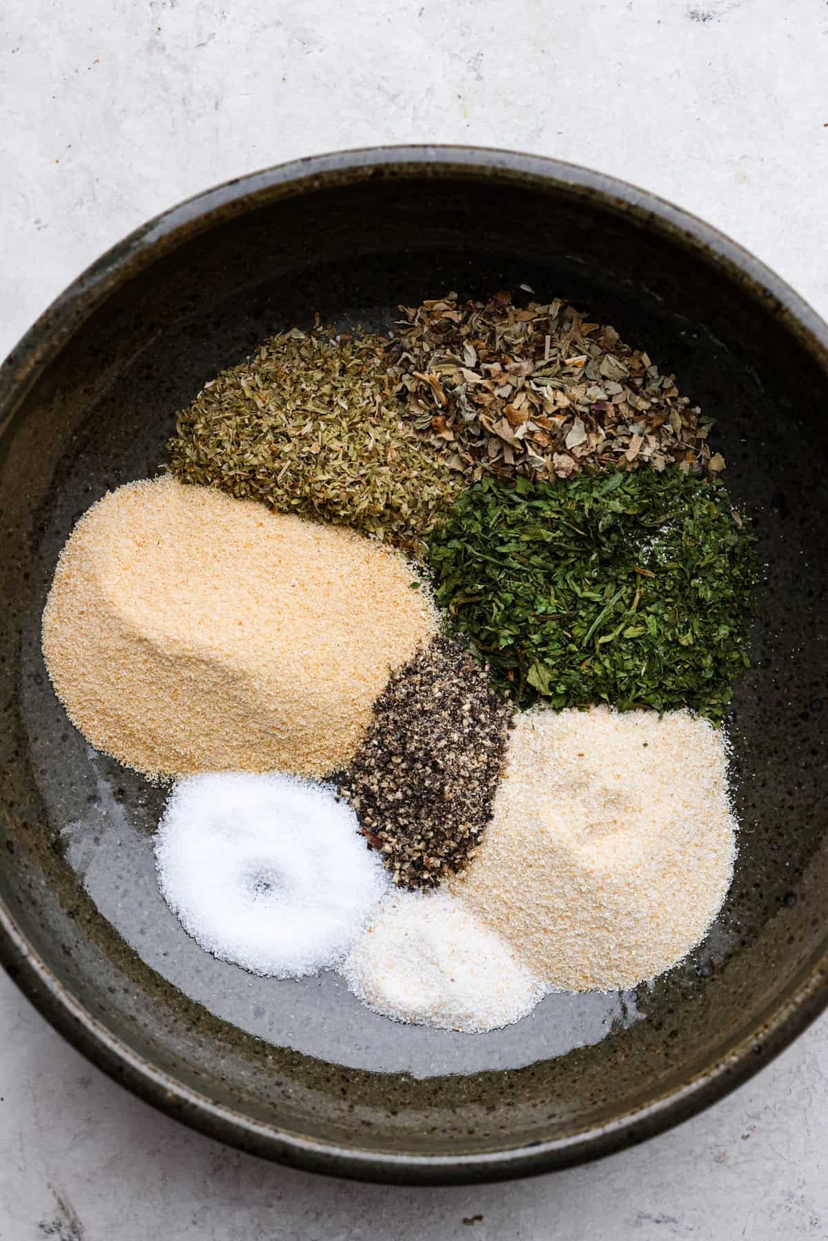 Homemade garlic herb seasoning is a great mix to have on hand. It has multiple uses, is full of flavor, and is adjustable to suit your taste preferences. It has the perfect mix of herbaceous dried herbs, garlic, onion powder, salt, and fresh cracked pepper. Overhead shot of each ingredient for homemade garlic herb seasoning in the same bowl in separate piles.