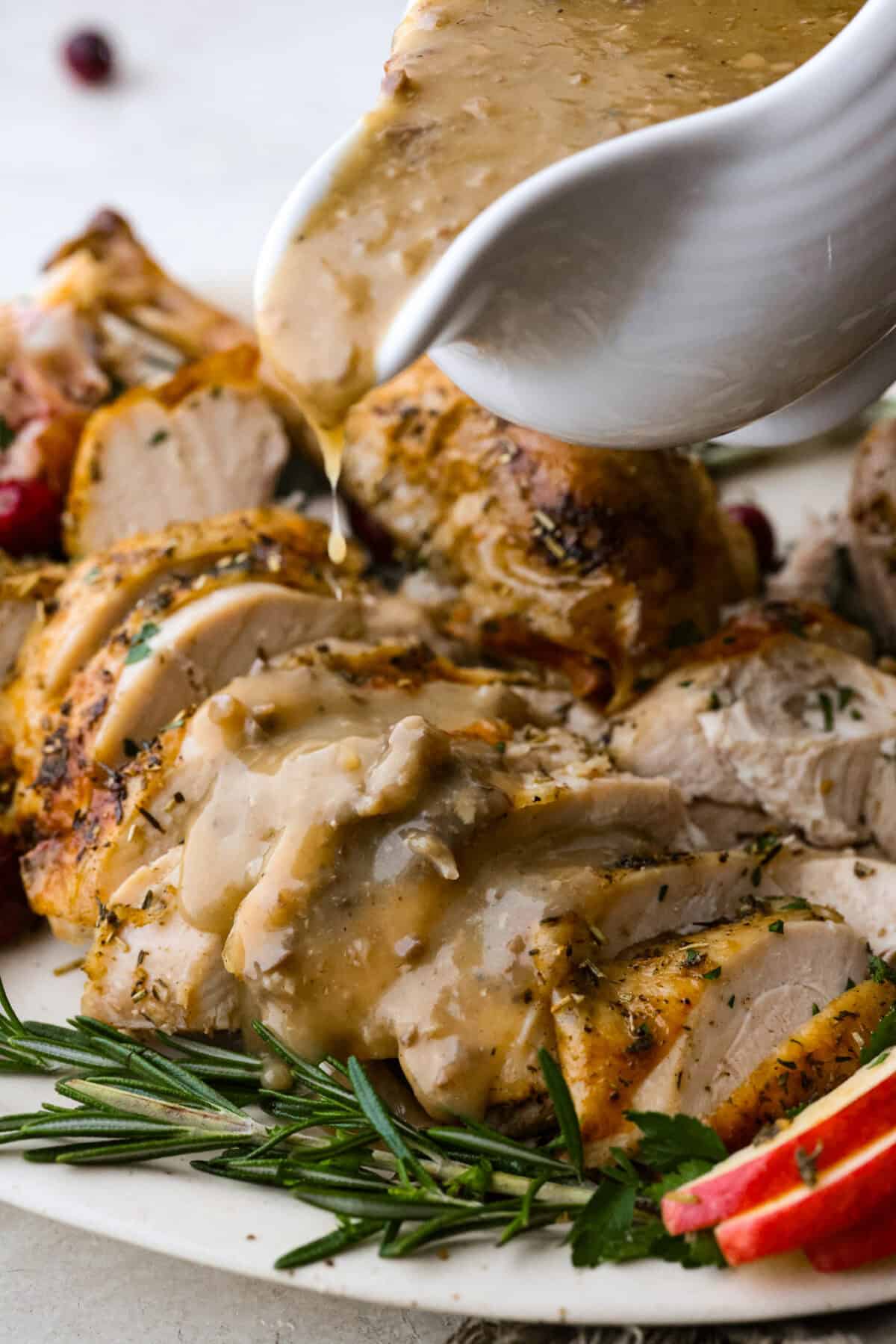 Side shot of someone pouring giblet gravy onto sliced turkey breast on a plate. 