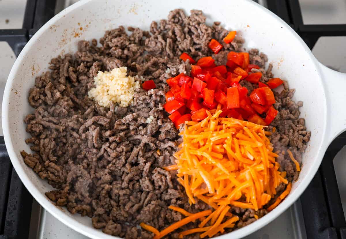 Overhead shot of browned beef with carrot shreds, red pepper and garlic on top. 