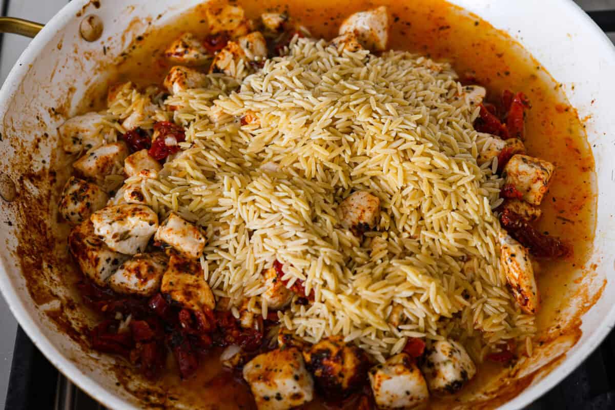 Overhead shot of orzo pasta being added to the chicken mixture in the skillet. 