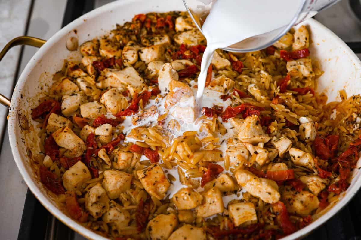 Overhead shot of the half-and-half being poured into the chicken mixture in the skillet. 