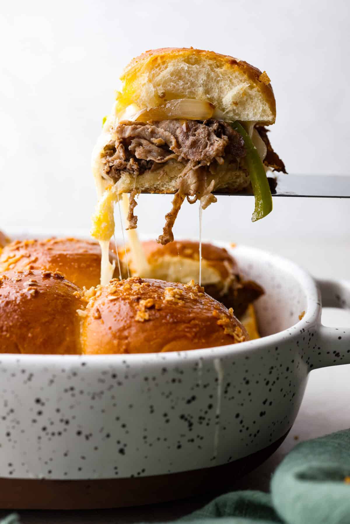 Side shot of a Philly cheesesteak slider being lifted out of the pan. 