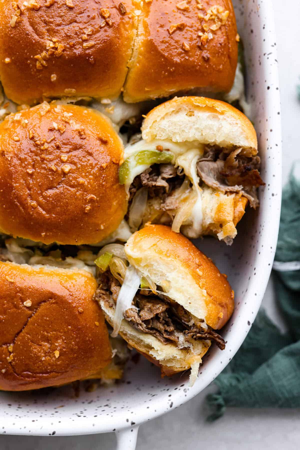 Overhead shot of Philly cheesesteak sliders in a baking dish with a couple of sliders turned on their side, 