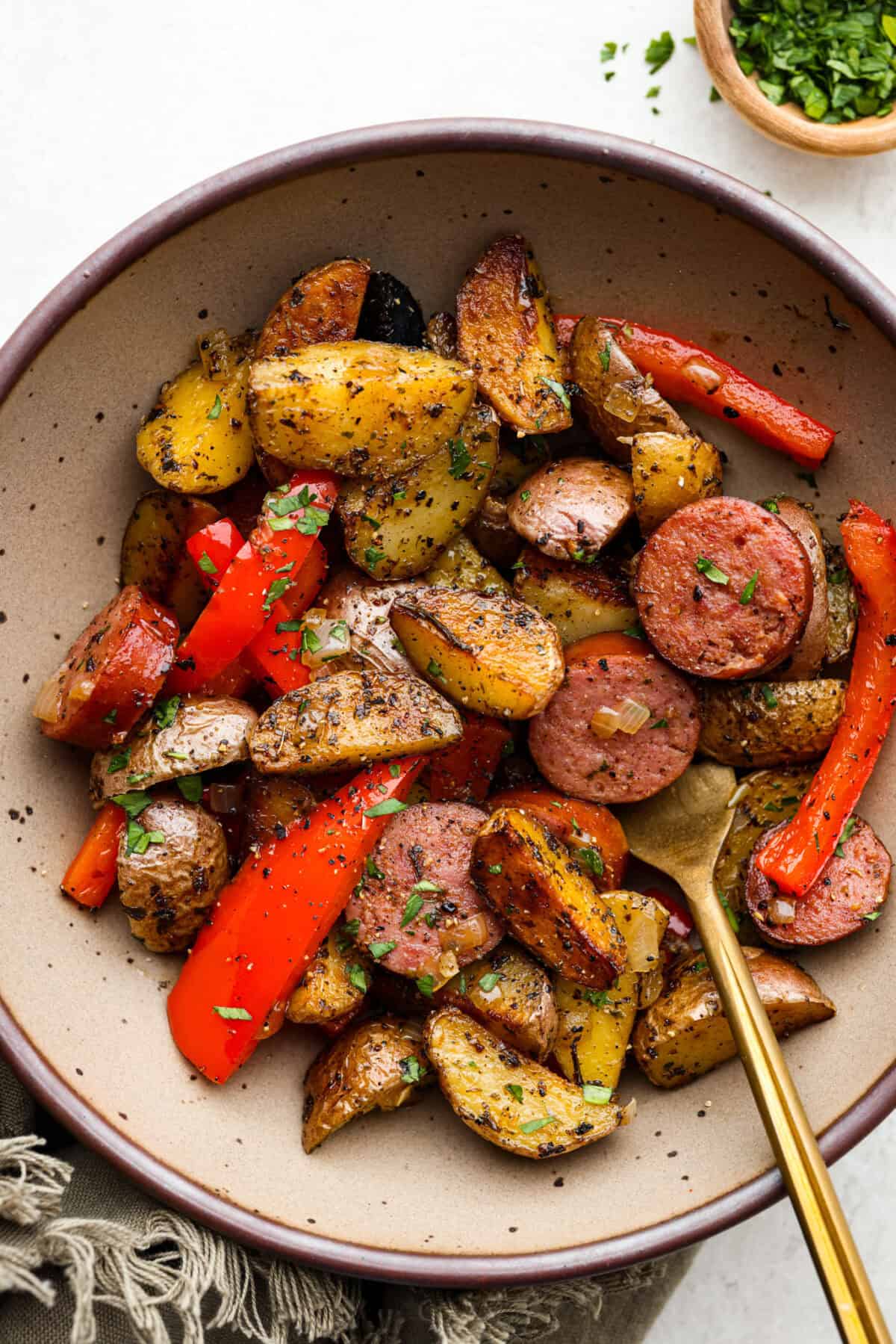 To view of sausage and potato skillet in a bowl with a gold fork.