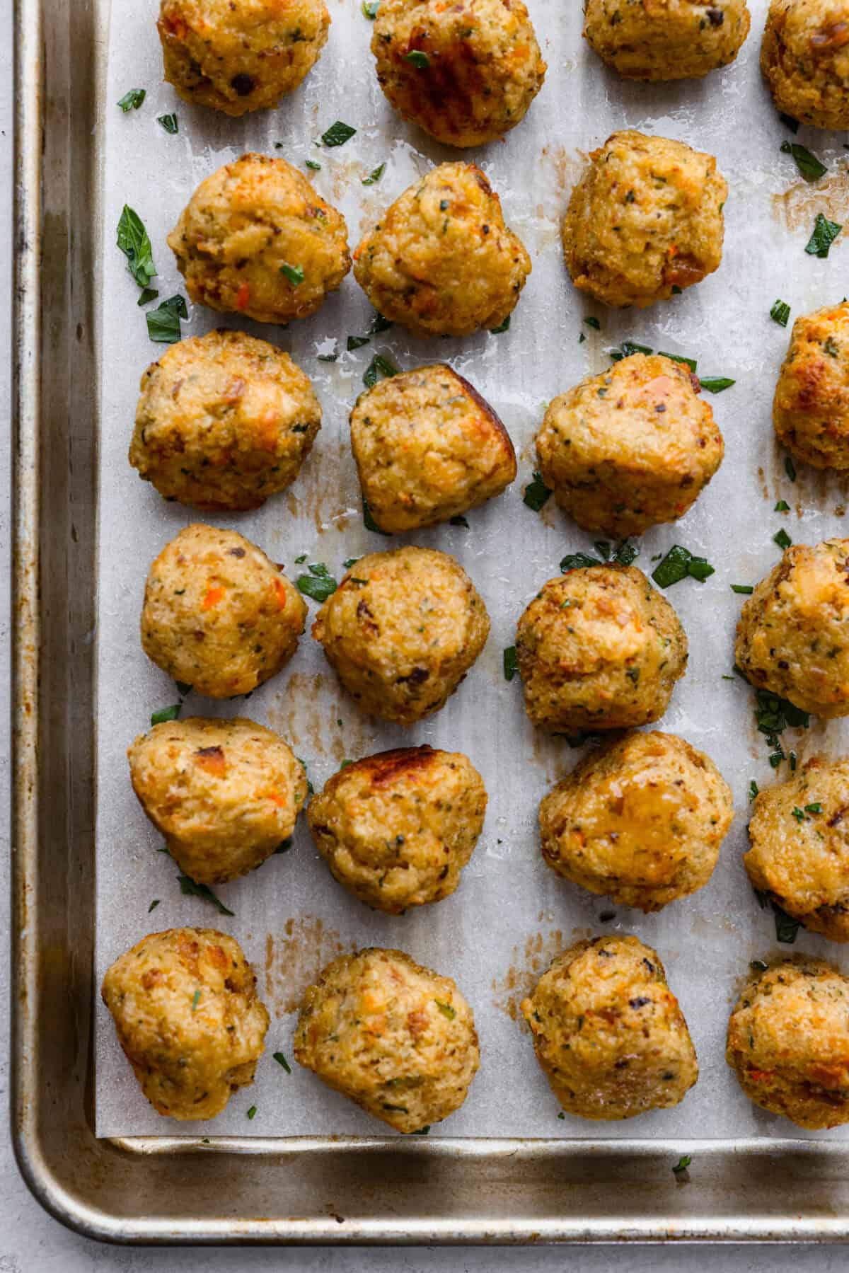 Overhead shot of cooked turkey stuffing balls on parchment paper on a cookie sheet. 