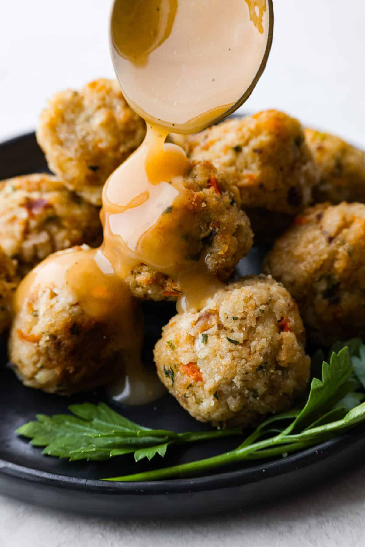 Close up shot of someone pouring gravy over turkey stuffing balls.