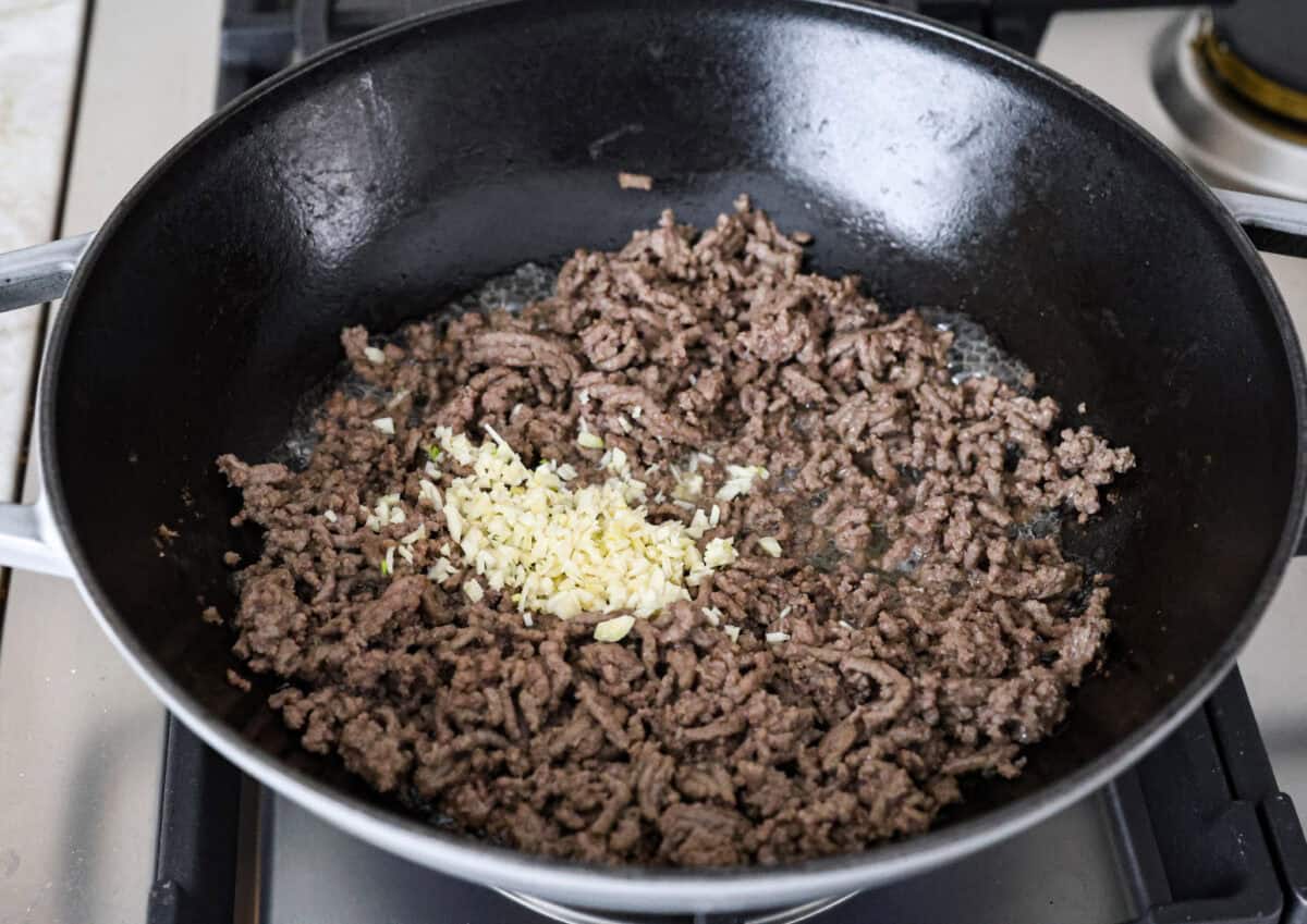 Angle shot of cooked ground beef in a skillet with minced garlic added on top. 