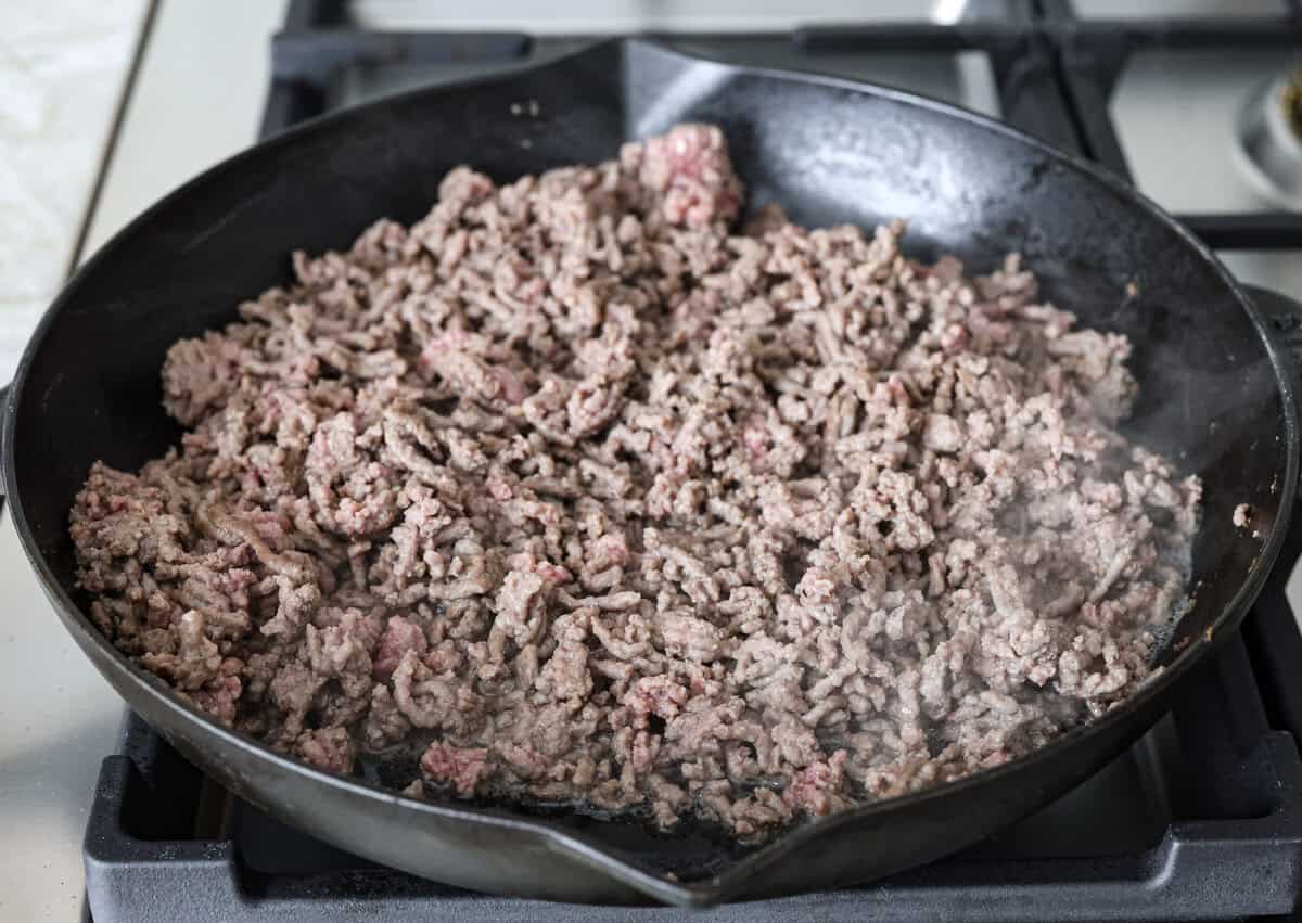 Salisbury Steak casserole is a warm and comforting savory dish. It has a thick beef gravy, tender mushrooms, and seasoned hamburger topped with rich, creamy potatoes. Angle shot of ground beef browning in a skillet.