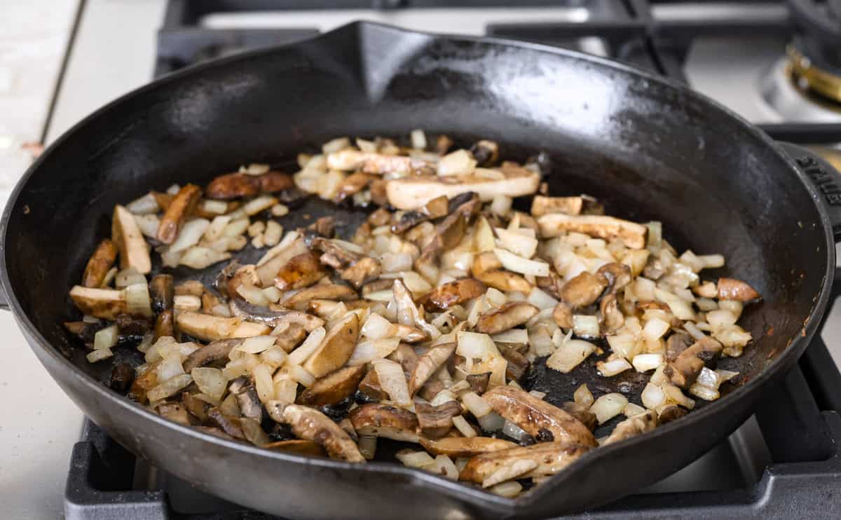 Salisbury Steak casserole is a warm and comforting savory dish. It has a thick beef gravy, tender mushrooms, and seasoned hamburger topped with rich, creamy potatoes. Angle shot of mushroom and onions cooking in the butter in a skillet.