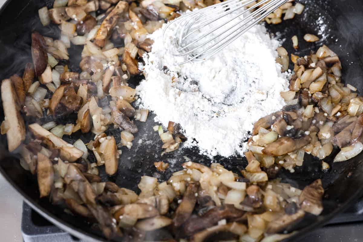 Salisbury Steak casserole is a warm and comforting savory dish. It has a thick beef gravy, tender mushrooms, and seasoned hamburger topped with rich, creamy potatoes. Angle shot of someone whisking flour into the mushroom butter and onion mixture.