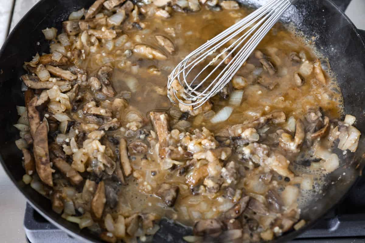 Salisbury Steak casserole is a warm and comforting savory dish. It has a thick beef gravy, tender mushrooms, and seasoned hamburger topped with rich, creamy potatoes. Overhead shot of someone whisking in beef broth into the vegetable roux.