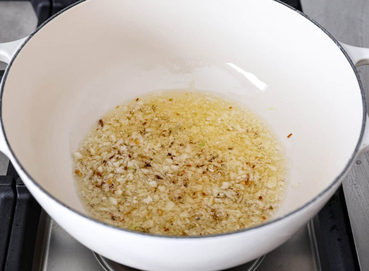 Angle shot of olive oil, garlic and red pepper flakes sautéing in a pot on the stove. 