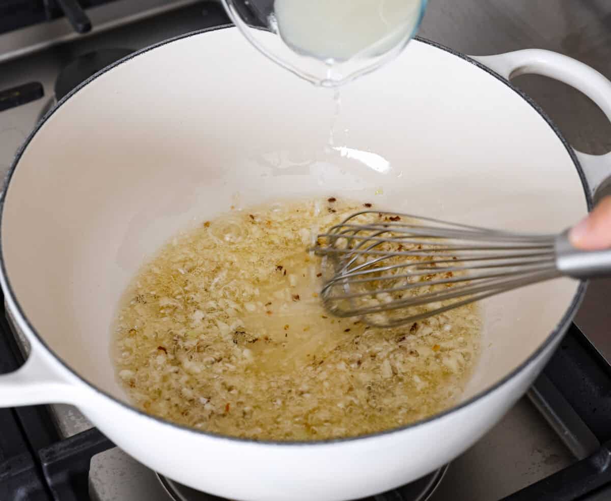 Angle shot of someone whisking the pasta water in with the olive oil, garlic and red pepper flakes. 