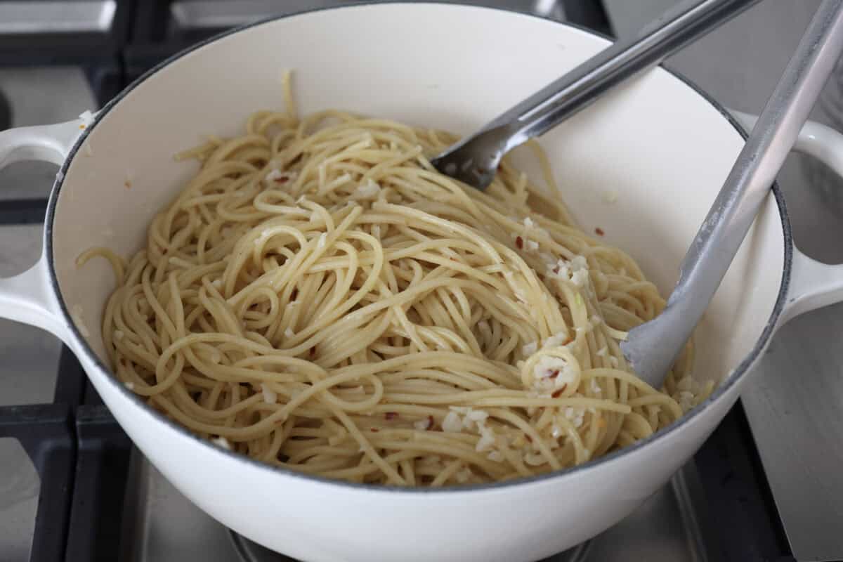 Angle shot of someone stirring noodles in the pot with the sauce. 