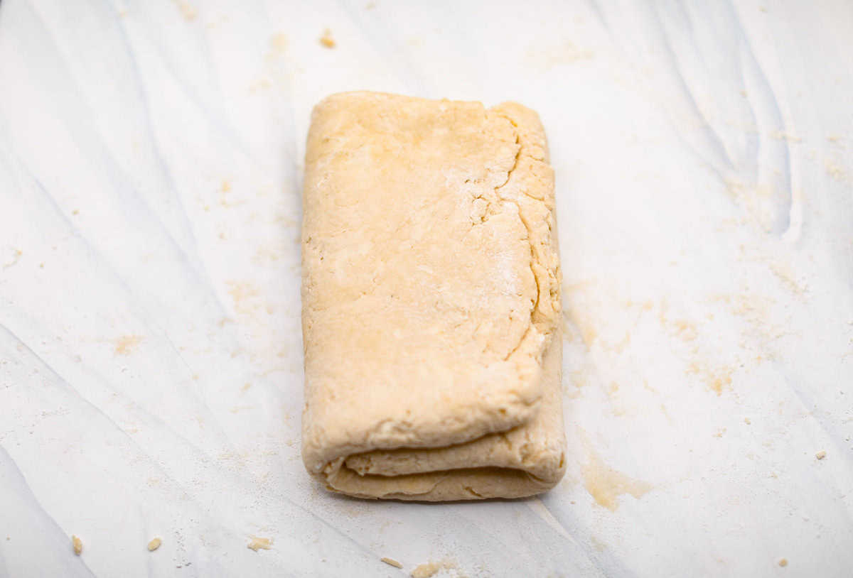 Biscuit Cinnamon Rolls are the most amazing twist on a classic! They are perfectly light, fluffy, and packed with cinnamon. The texture is more flakey and moist than traditional cinnamon rolls! Whether it’s for a cozy weekend breakfast or a holiday brunch, these hit the spot! Overhead shot of biscuit dough folded into a tri-fold.