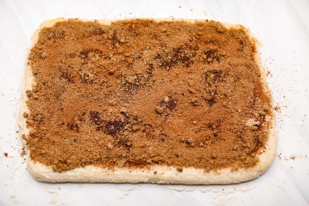 Overhead shot of the cinnamon and brown sugar mix spread over the butter on the rolled out dough. 