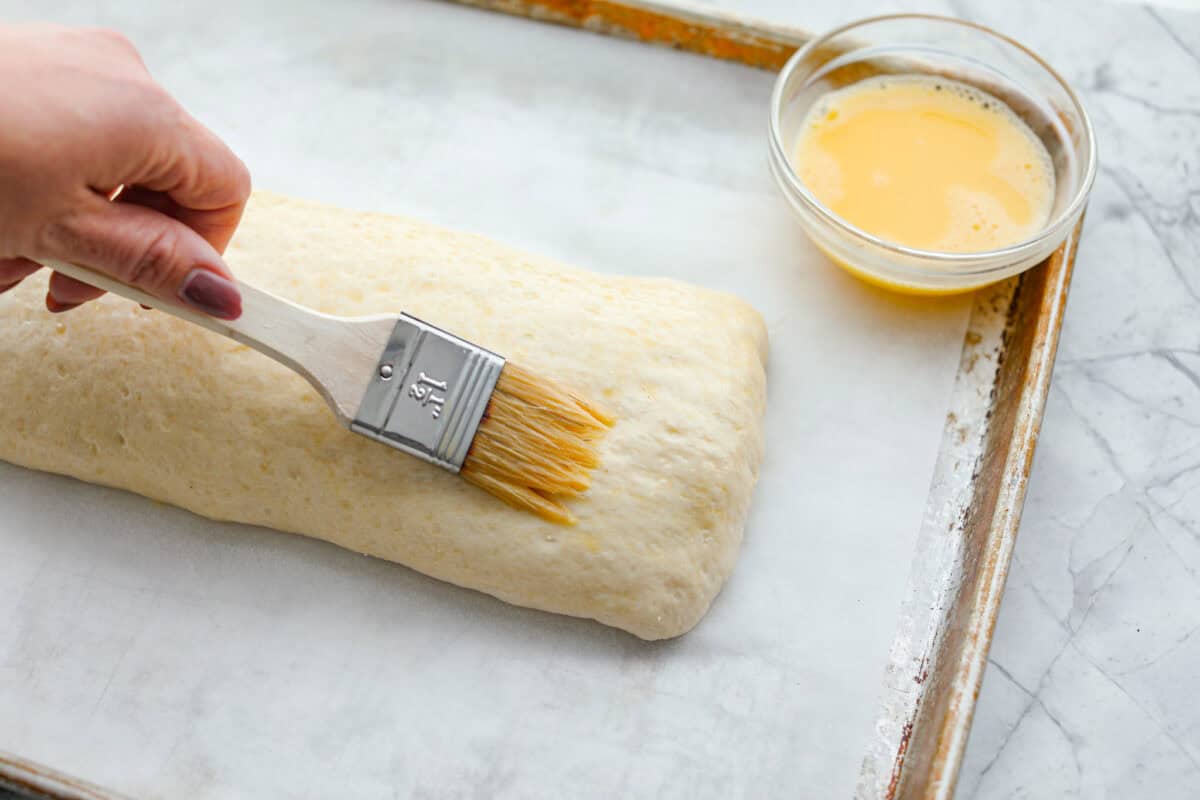 Angle shot of someone spreading the gg wash on the Stromboli. 