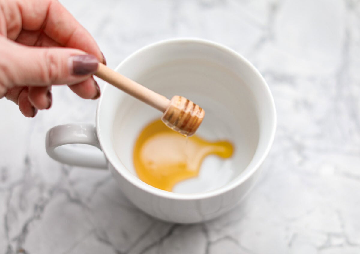 Overhead shot of someone putting honey in the bottom of a mug. 