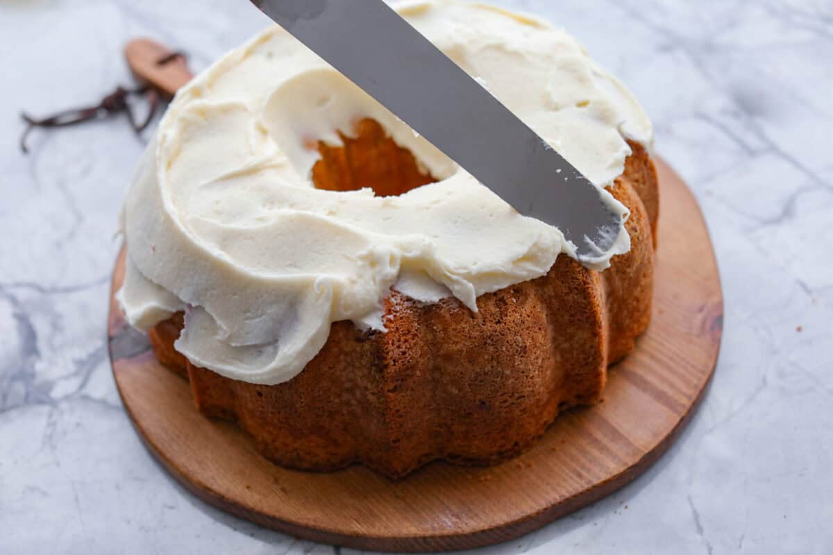 Angle shot of someone spreading the frosting on the cooked bundt cake. 