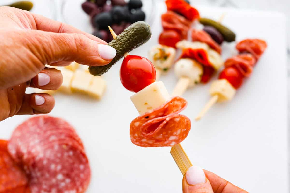 Second photo of a pickle going on a skewer full of tomato, cheese, and pepperoni.