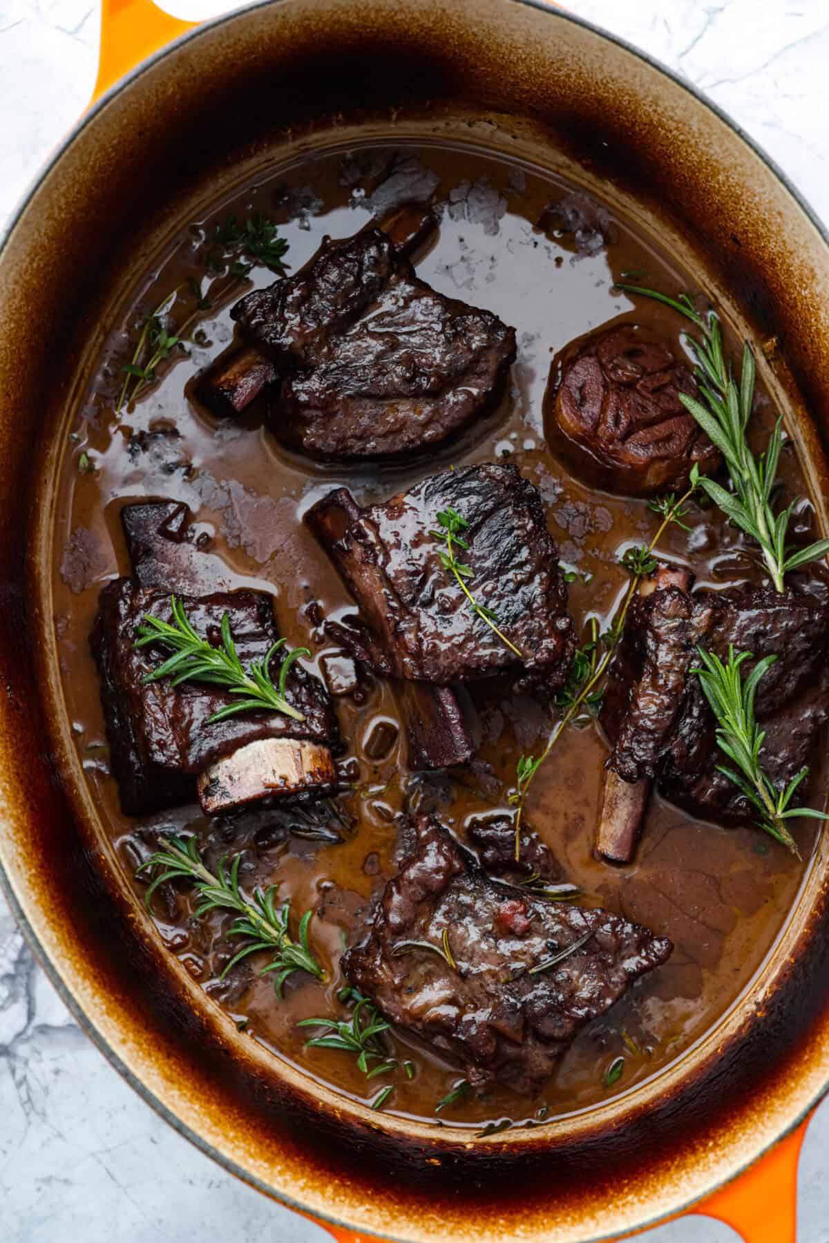 Top view of braised short ribs in a dutch oven pot garnished with herbs.