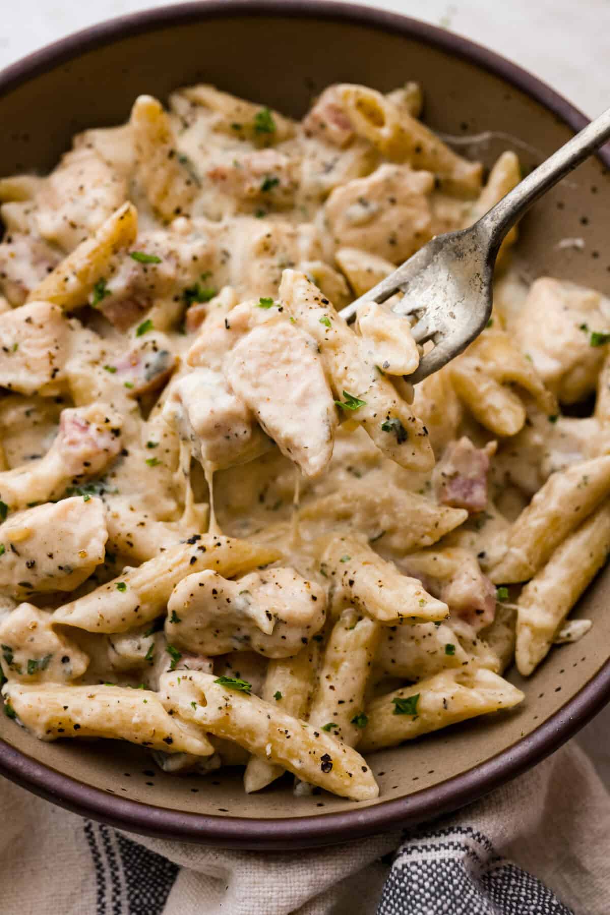 Close up shot of a fork full of a bite chicken cordon bleu pasta. 