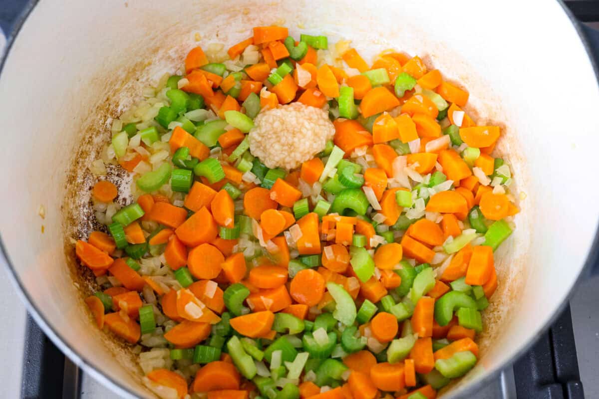 Overhead shot of carrots, celery and onions in the bottom of a pot with garlic on top. 