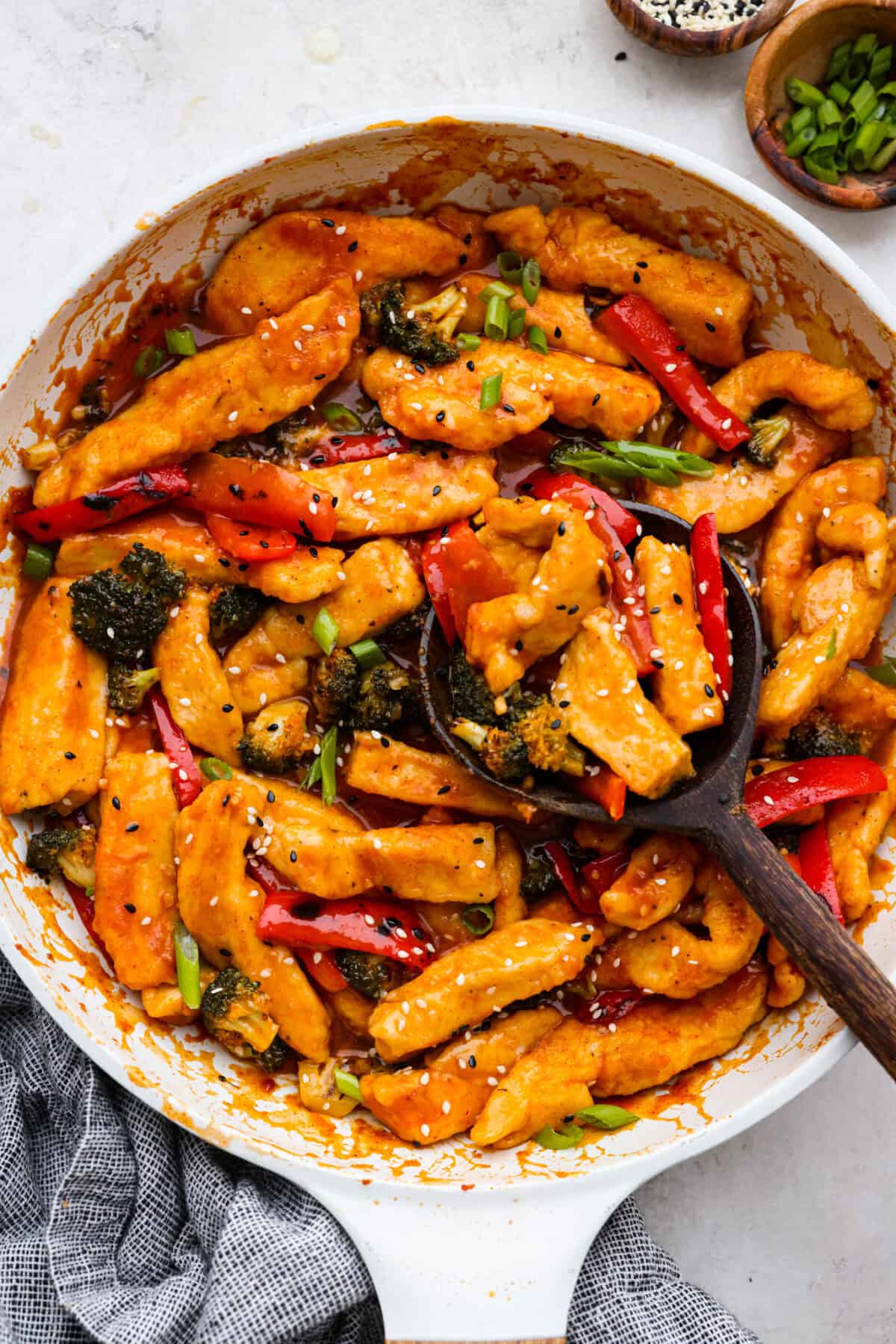 Top view of Hunan chicken in a white skillet with a wood serving spoon.