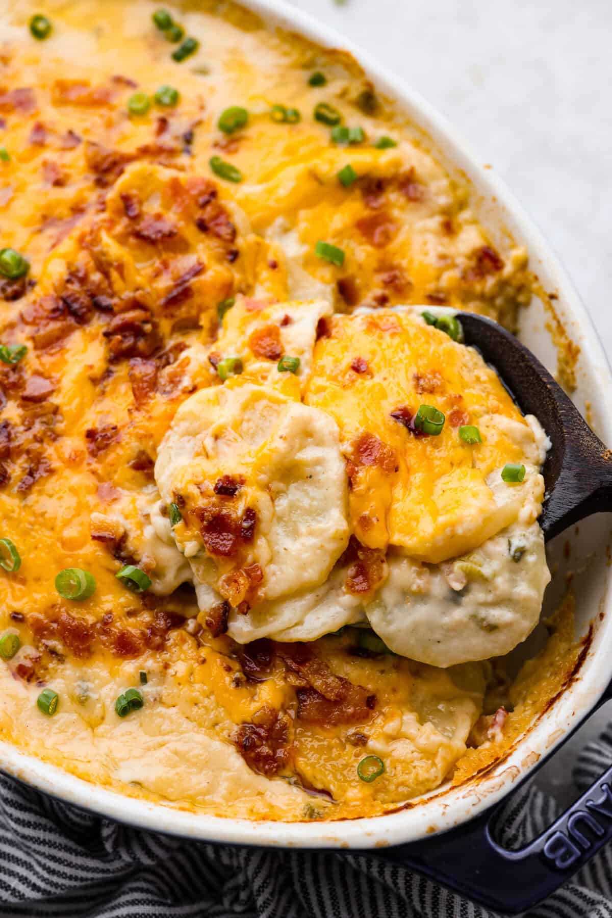 Angle shot of someone scooping out a serving of loaded scalloped potatoes. 