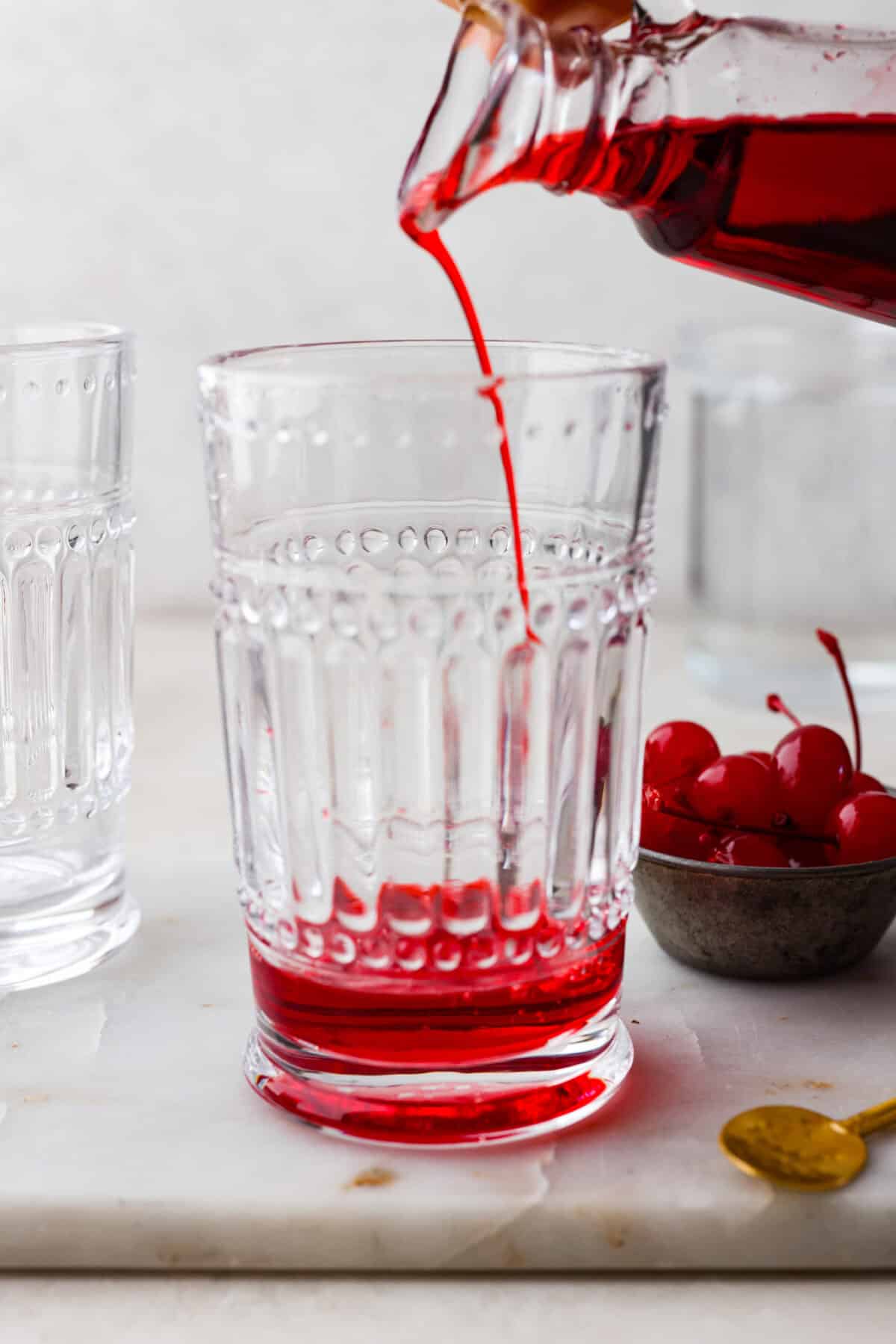 Side shot of someone pouring grenadine  into the bottom of a glass. 