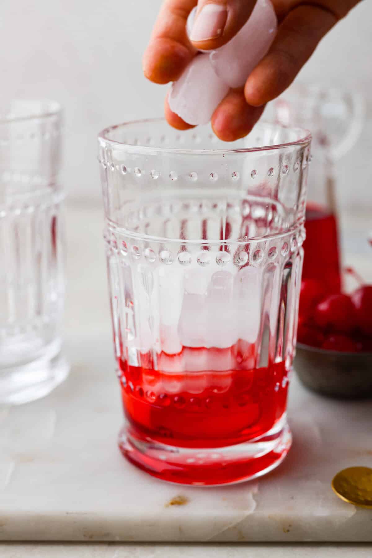 Side shot of someone putting ice into the glass with grenadine. 