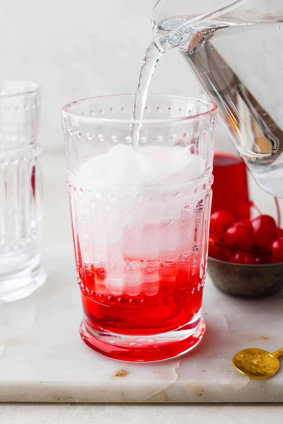 Side shot of someone pouring soda into the ice and grenadine to complete their Shirley Temple. 