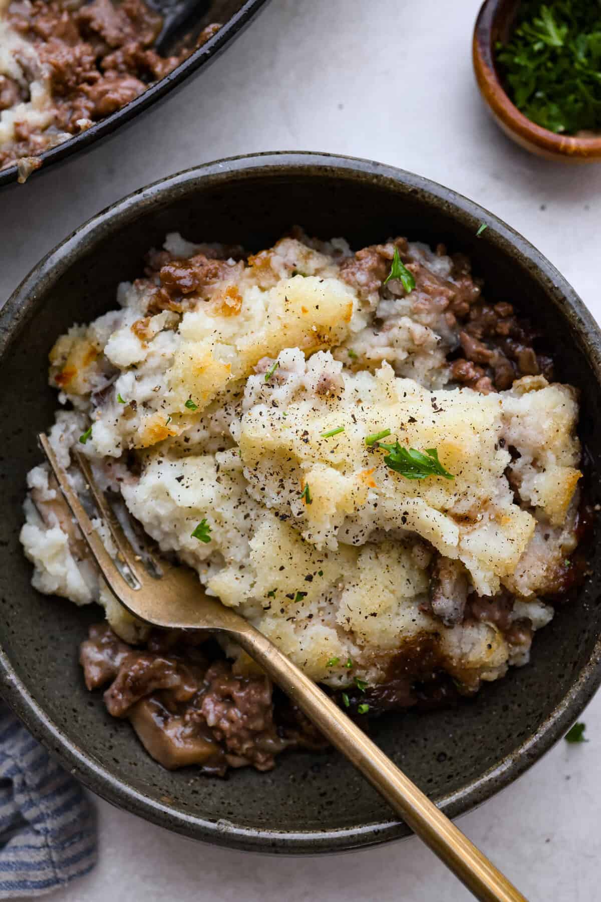 Salisbury Steak casserole is a warm and comforting savory dish. It has a thick beef gravy, tender mushrooms, and seasoned hamburger topped with rich, creamy potatoes. Overhead shot of plated salisbury steak casserole.