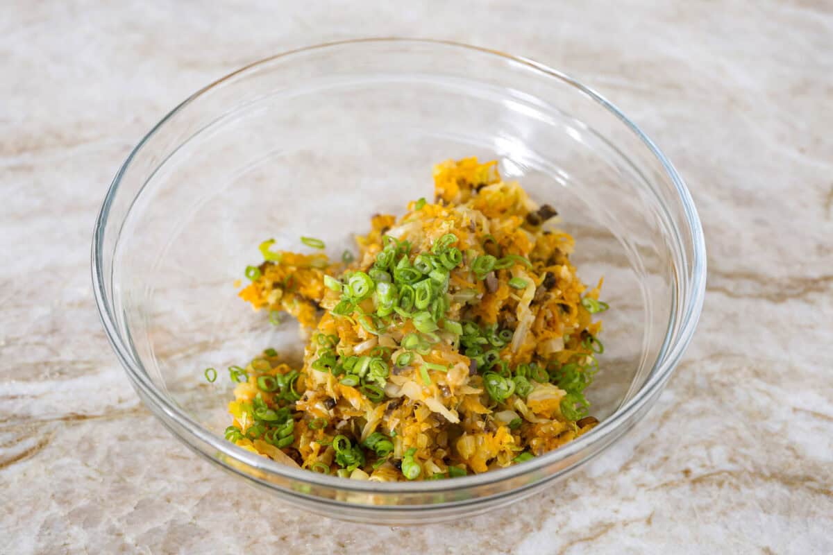 Angle shot of a bowl with the cooked veggies and green onion and soy sauce added in. 