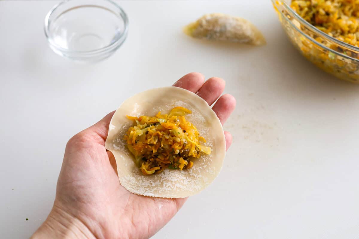 Angle shot of someone holding a dumpling wrapper with some of the filling in the middle. 