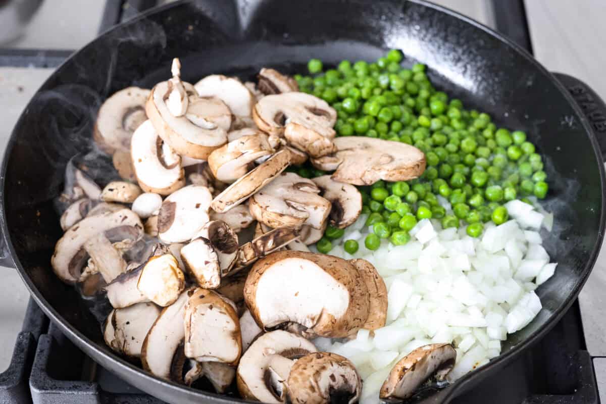 Overhead shot of the butter, mushrooms, onion and peas cooking in a skillet. 