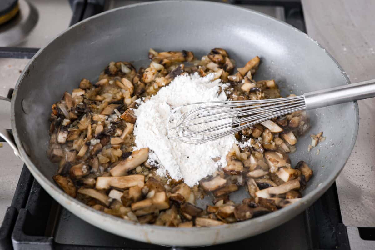 Angle shot of someone whisking the flour into the mushrooms and onions. 