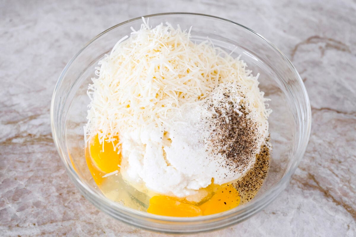 Overhead shot of ricotta, parmesan, eggs, salt and pepper in a bowl.