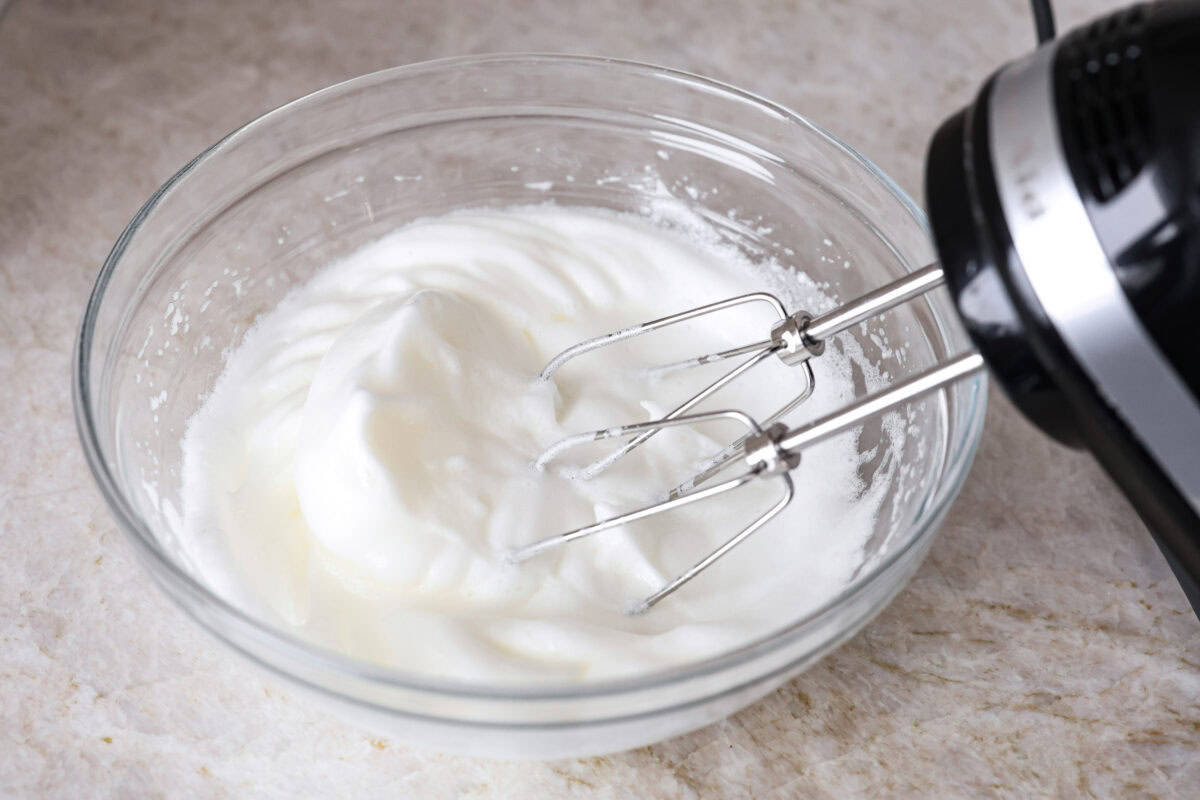 Angle shot of someone using a hand mixer to whisk egg whites in a bowl.