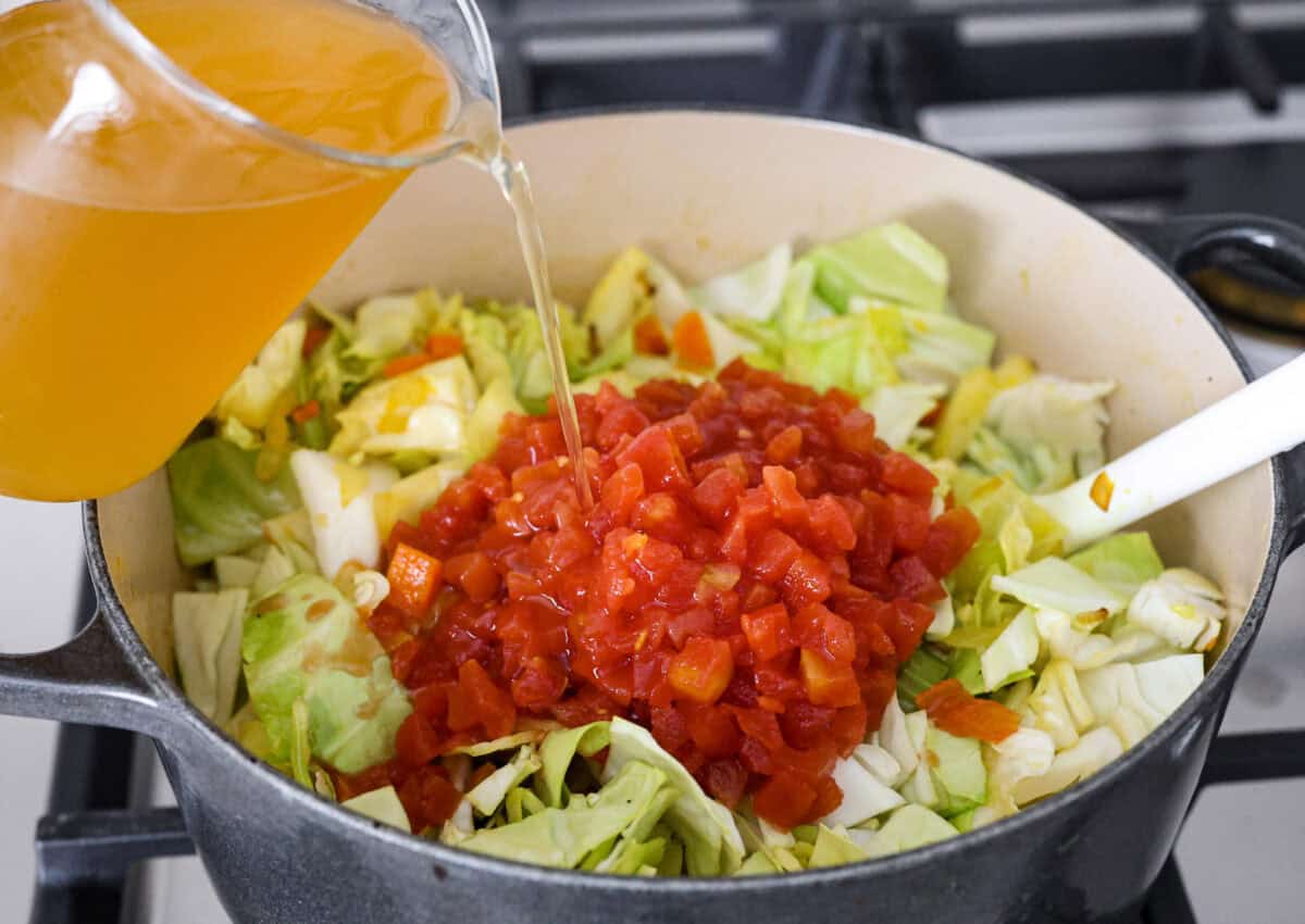 Angle shot of the vegetables, seasonings and cabbage with the tomatoes and vegetable broth on top. 