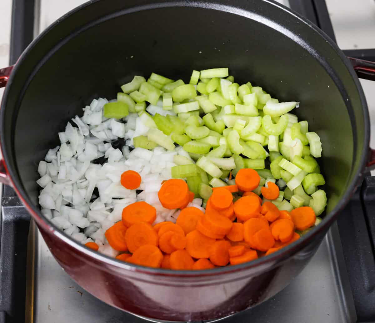 Overhead shot of celery, onions and carrots in a pan with olive oil. 