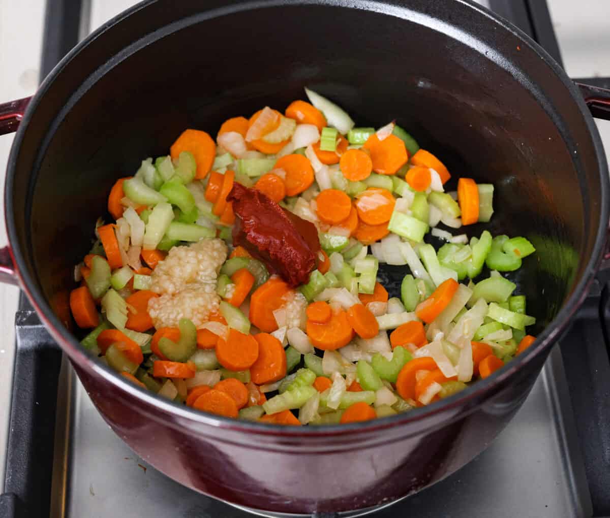 Overhead shot of partially cooked vegetables with added garlic and tomatoes. 