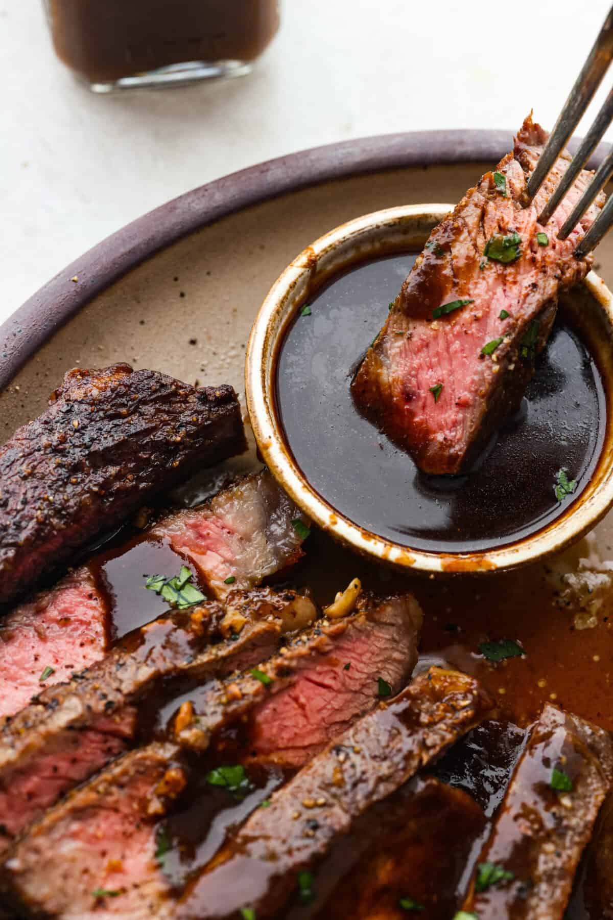 Angle shot of someone dipping a piece of steak into the homemade steak sauce.