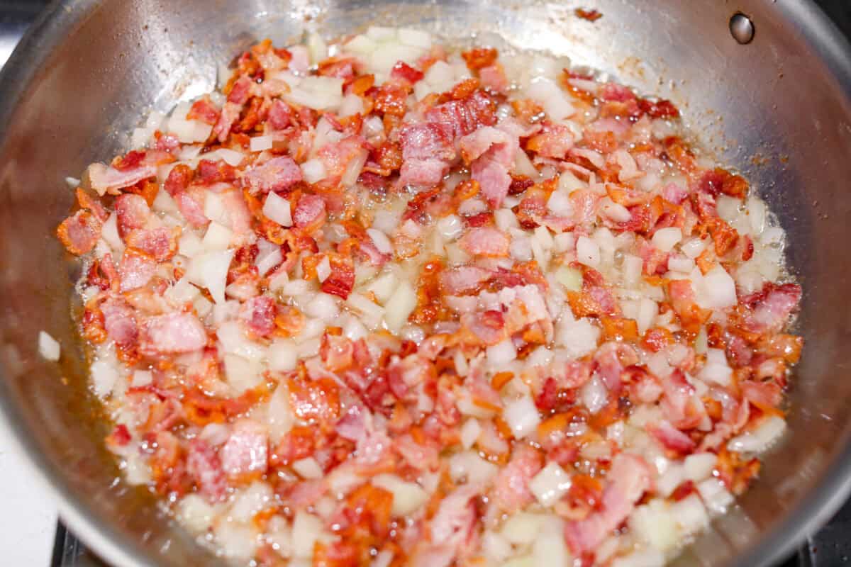 Overhead shot of bacon and onions cooking together in a skillet. 