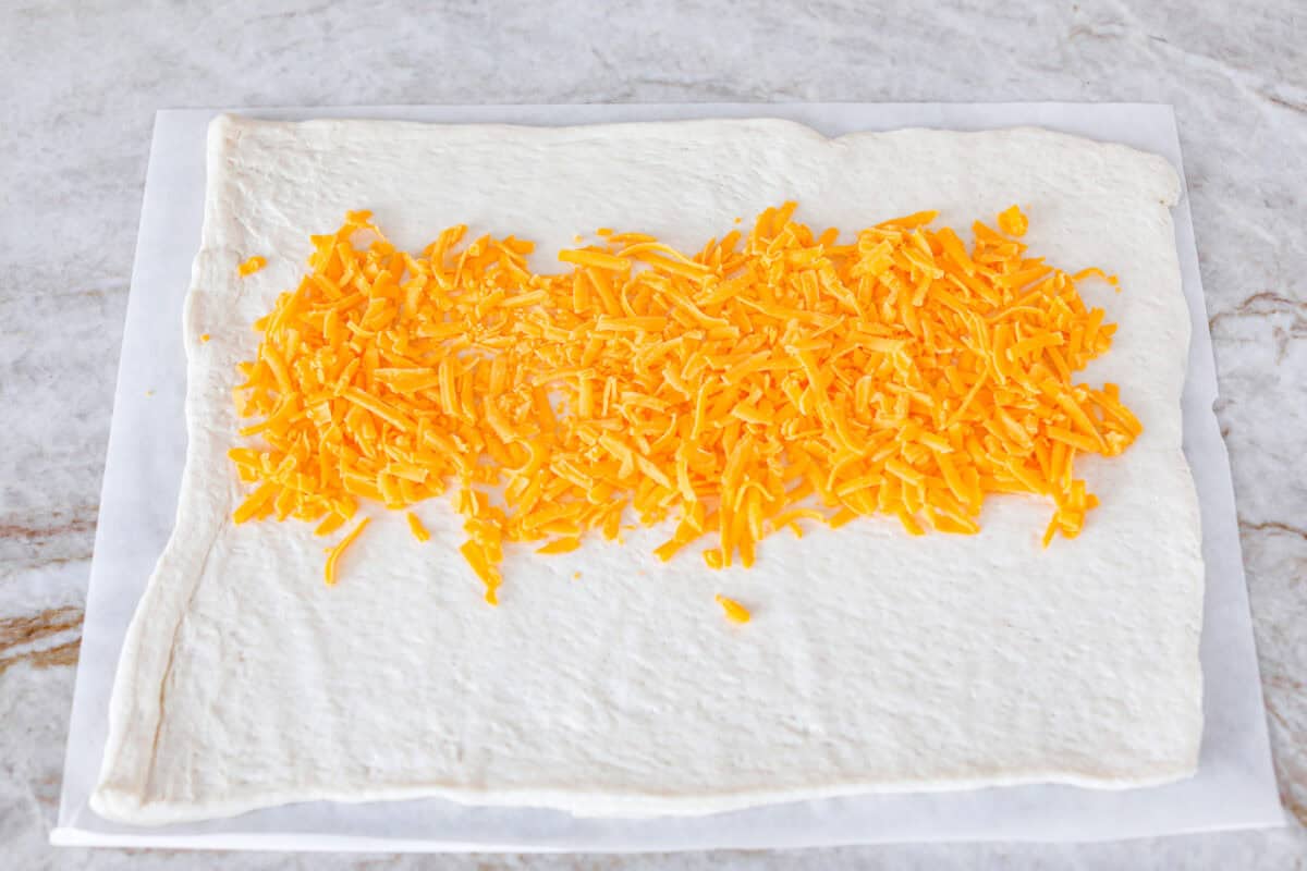 Overhead shot of the pizza crust dough rolled out onto parchment paper with cheese sprinkled through the middle. 