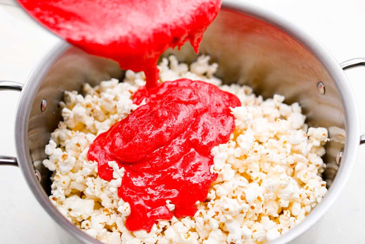 Angle shot of someone pouring the candy and butter mixture over the popcorn. 