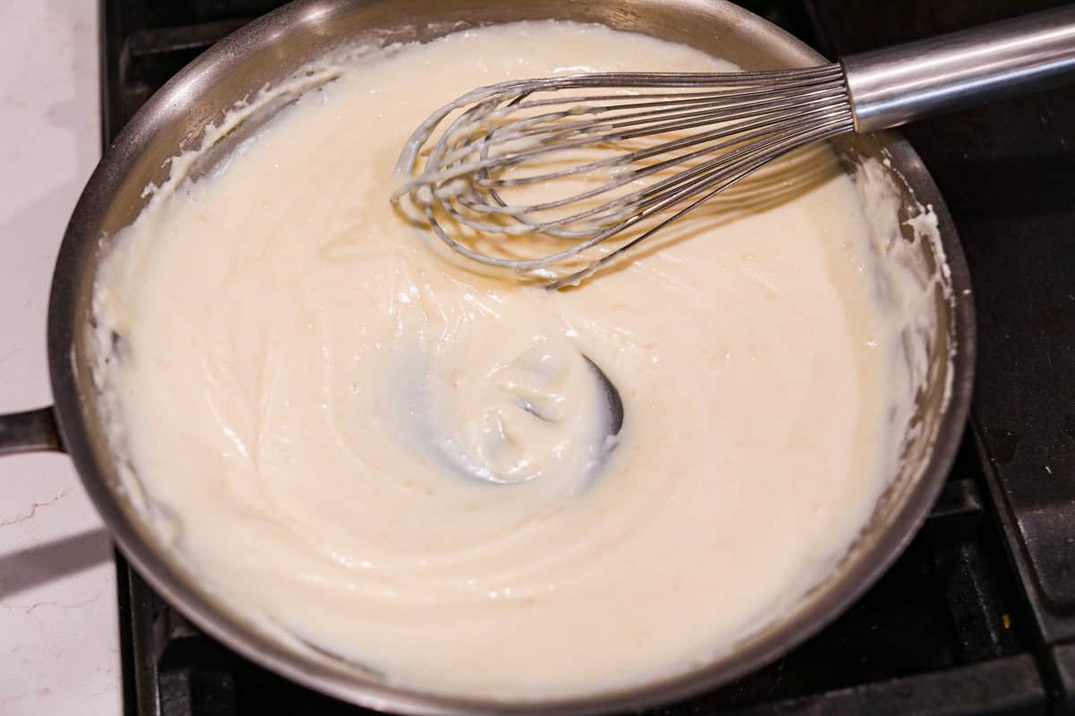 Loaded scalloped potatoes are rich, creamy, and Angel shot of someone whisking the milk and sour cream into the roux.