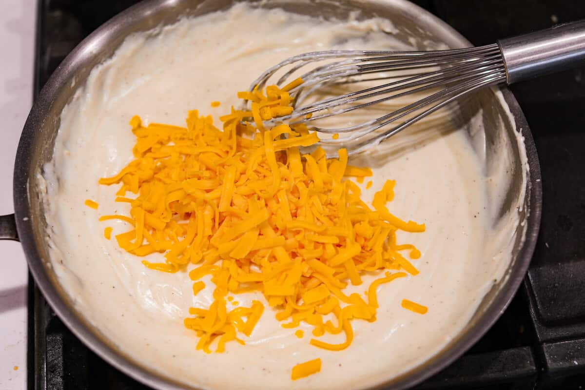 Loaded scalloped potatoes are rich, creamy, and Angle shot of someone whisking the cheese into the sauce.